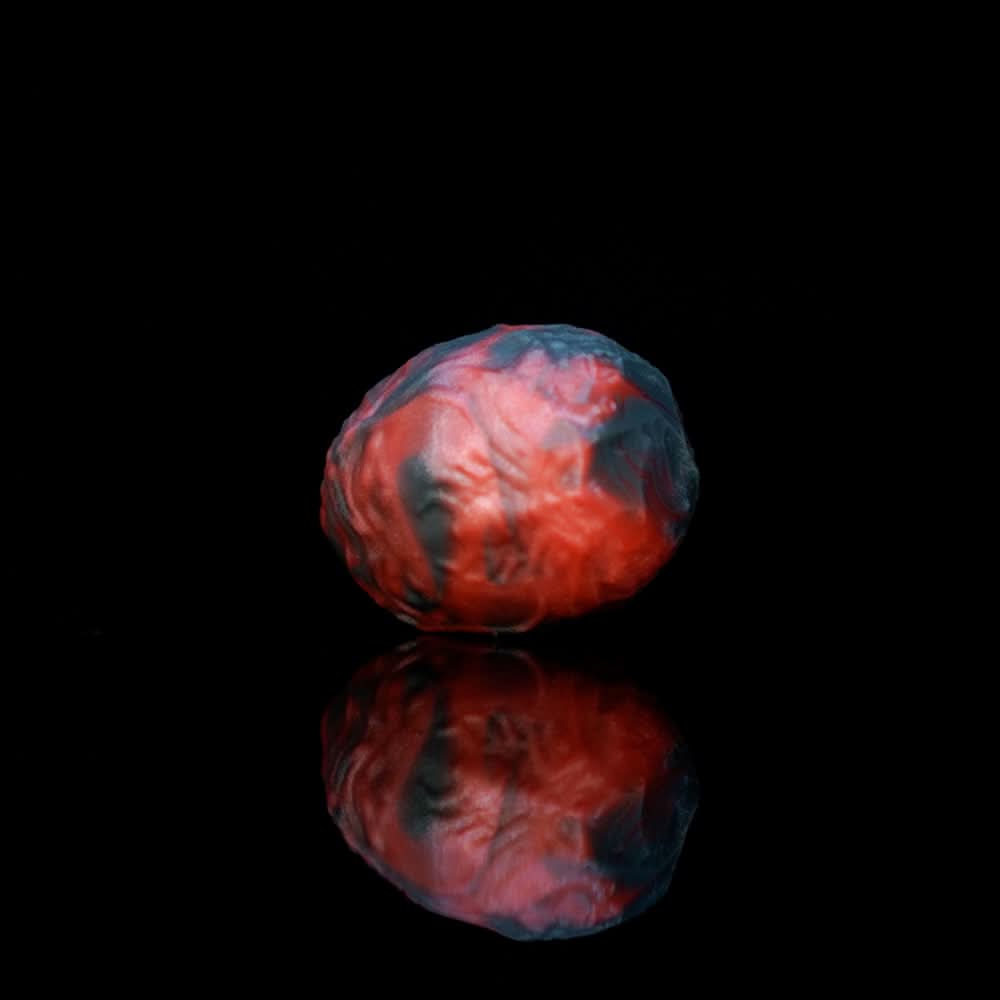 Marbled black and red monster egg insert held between fingers for scale.